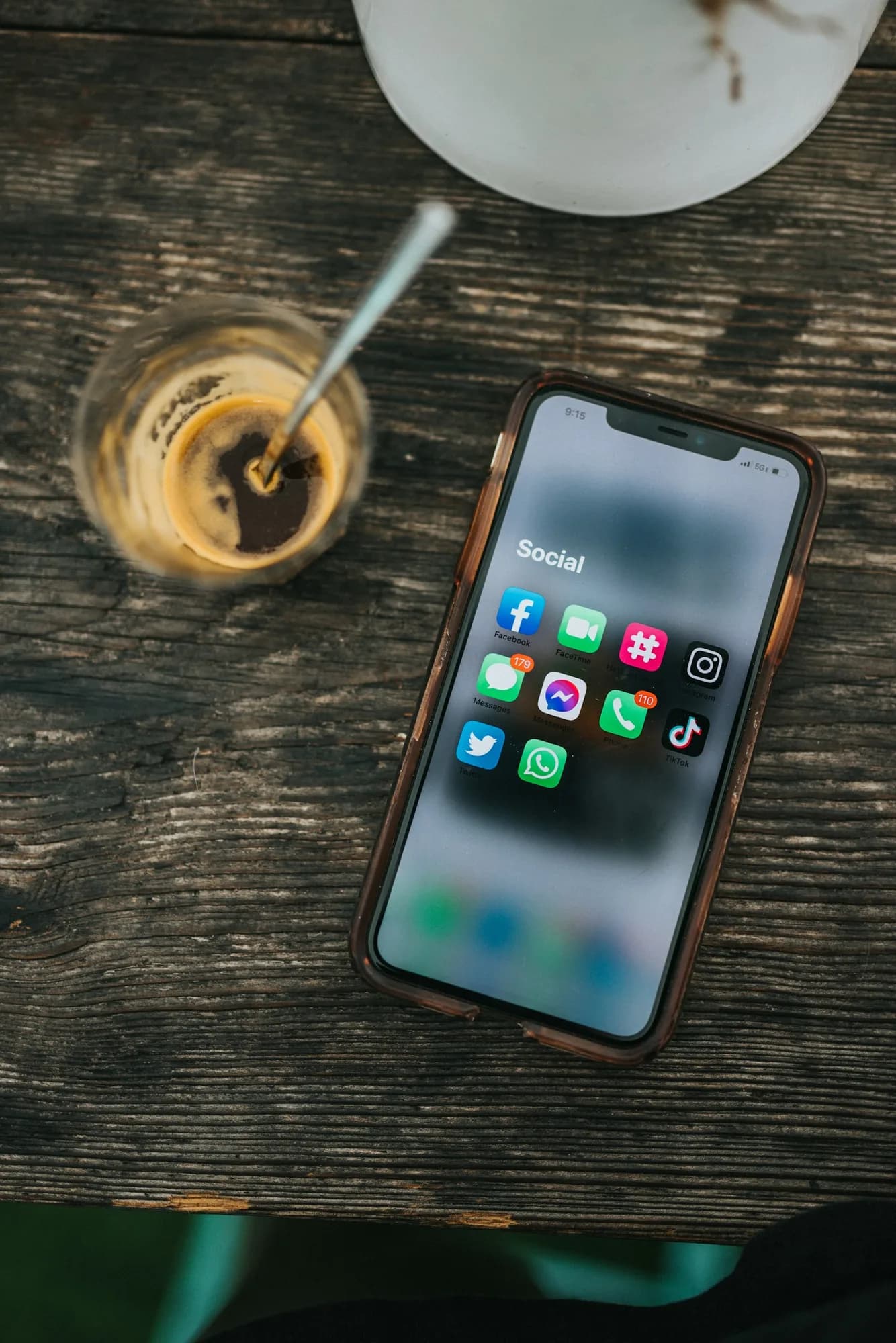 A smartphone showing social media apps on a wooden table beside a coffee glass